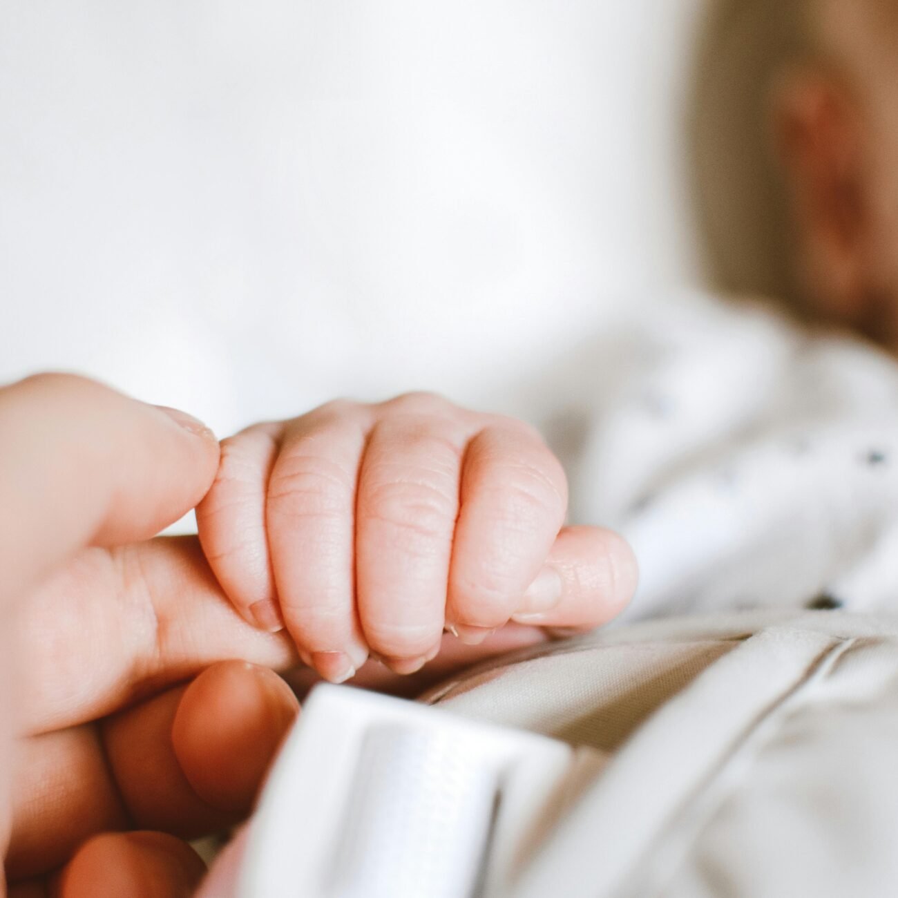 Close-up of a newborn's hand gently gripping a parent's finger, symbolizing love and connection.