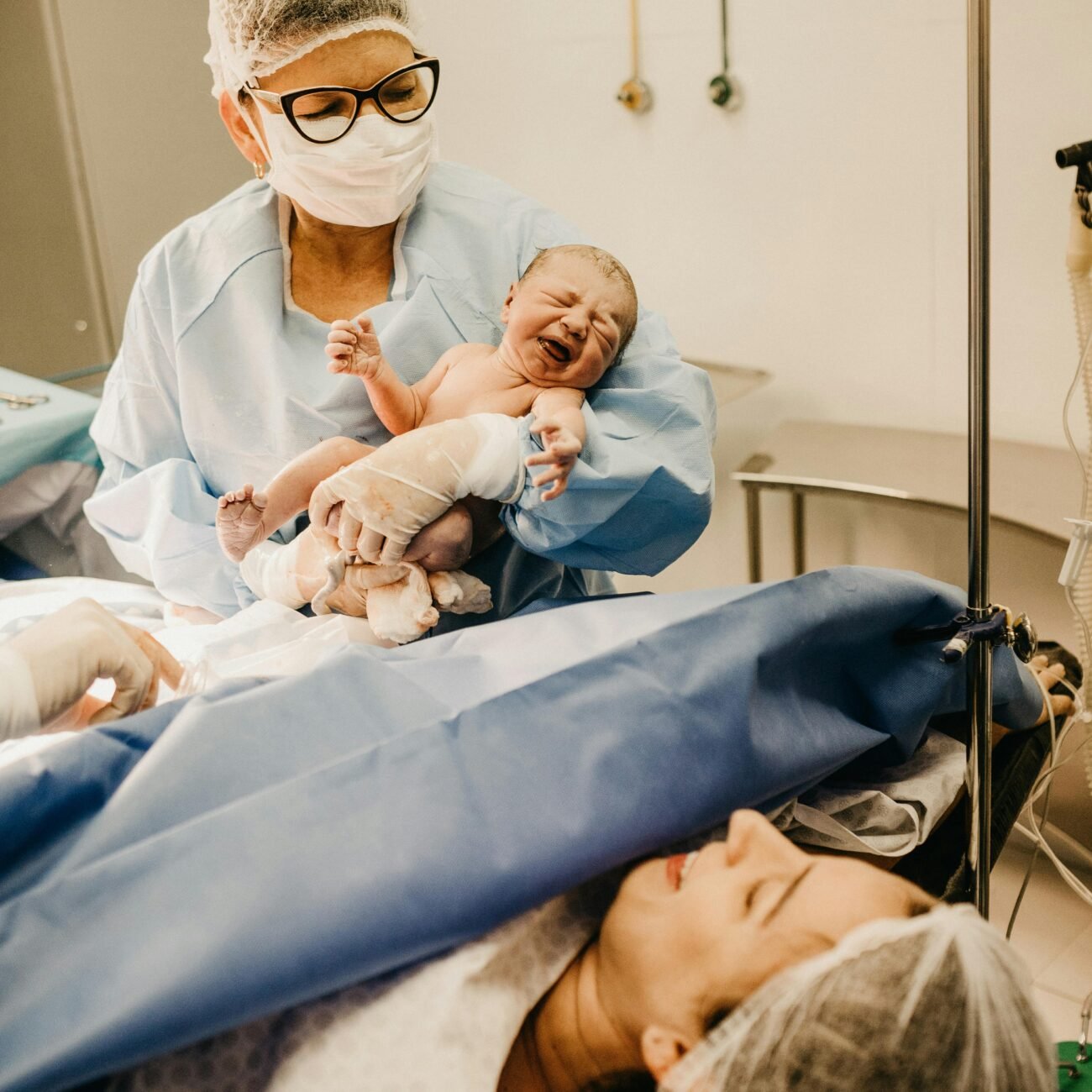 A doctor holds a newborn baby in a hospital setting post-delivery.